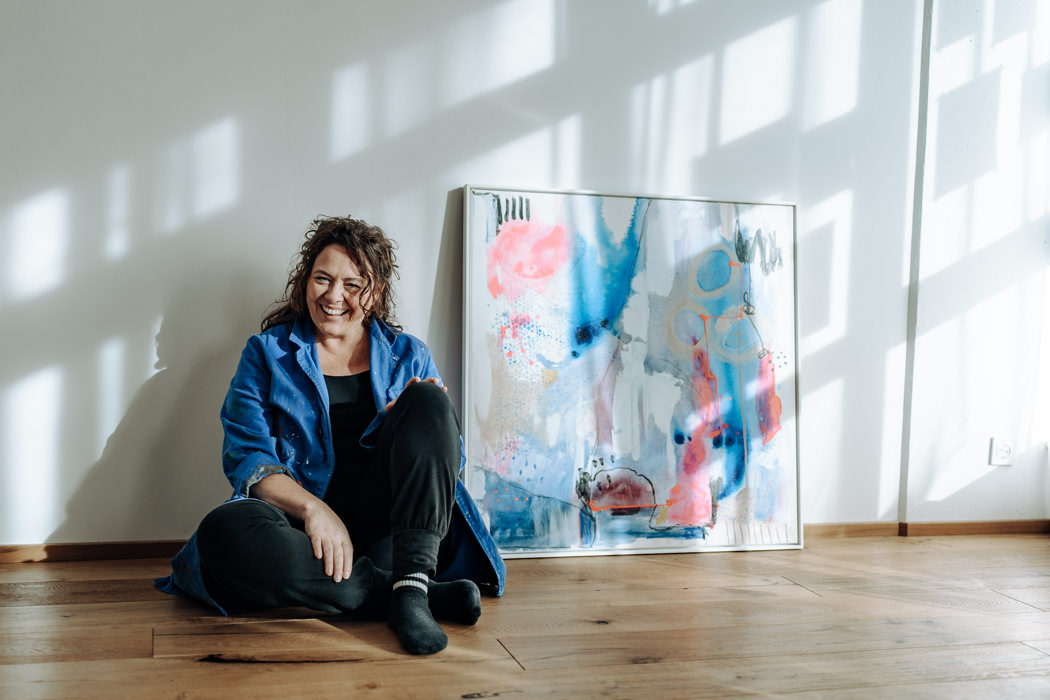 Brand Foto einer Künstlerin in Freiburg neben ihrem Gemälde und mit Licht und Schattenspiel im Hintergrund.